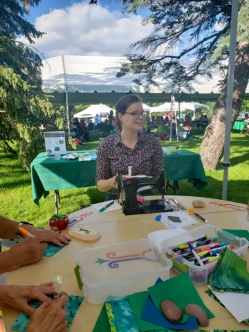 20220821_172212 Image of the artist, Stephanie Lynn Rogers, sitting in front of a compact vintage sewing machine in a park setting.