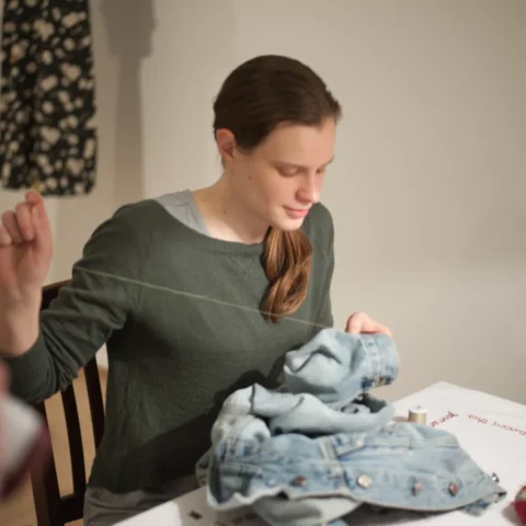 Alterations_Alterations-53 copy A person hand sews something onto a denim jacket