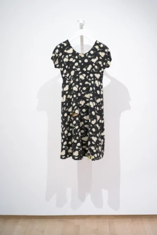 Dress made of fabric with a black background with white polka dots and daisies. There are insects appliqued on top.