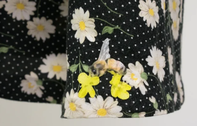 Close-up of the hem of a dress showing an appliqued bee on yellow flowers against a black background with white polka dots and daisies.