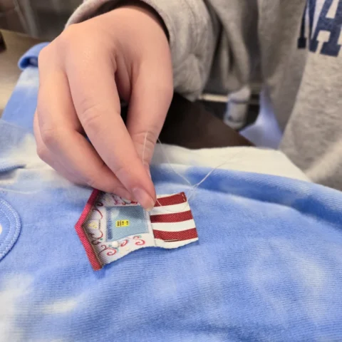 Amendments_20240410_094452 copy close-up of someone handsewing a fabric patch that looks like the Granite Falls Kiwanis pop-corn stand
