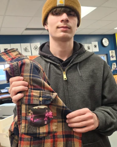 Amendments_20240410_111702 copy participant holds up a flannel shirt with an image of the footbridge in downtown Granite Falls sewn to the chest pocket