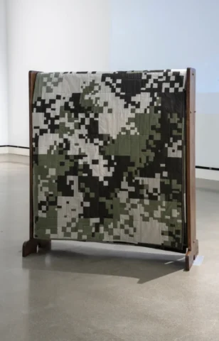 aov9_stephanierogers_dsc0201_31976288388_o A quilt pieced into a digital camouflage pattern in shades of tan, olive green, and dark brown folded neatly on a quilt rack.