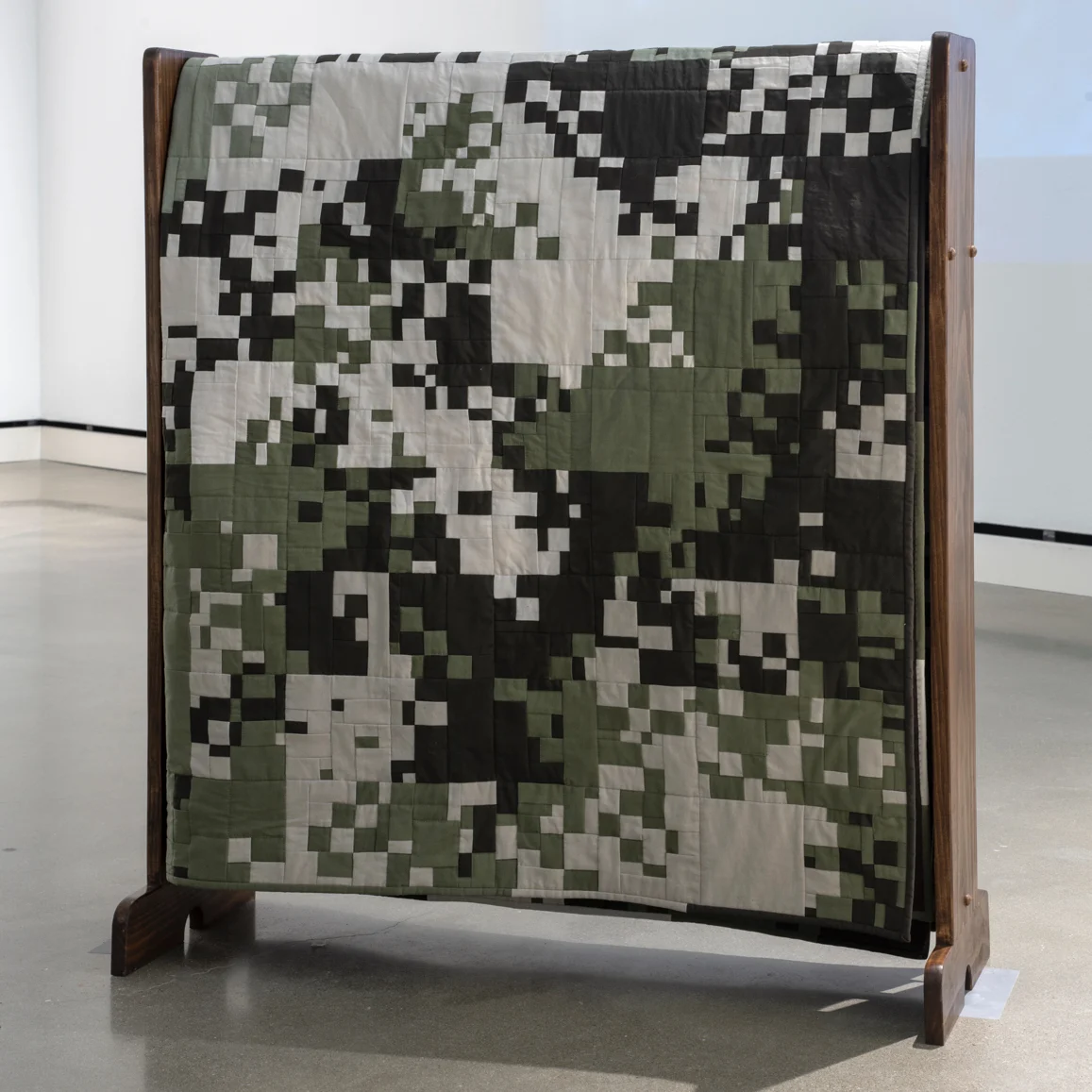 Intricately pieced quilt with digital camouflage pattern on a quilt rack by Stephanie Lynn Rogers