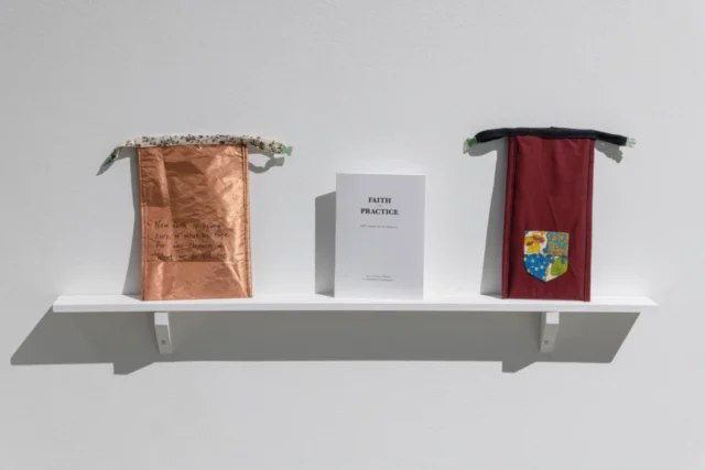 aov9_stephanierogers_dsc0214_45847211591_o A small shelf holds two pouches (one copped and one dark red with a patchwork shield) and a zine titled "Faith and Practice"