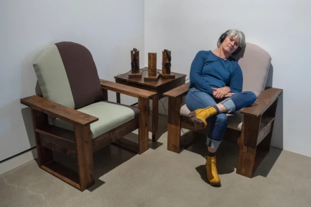 aov9_stephanierogers_dsc0899-1_44030412380_o A woman sits sideways in a large lounge chair. She is listening to one of three headshets that rest on the adjacent side table.